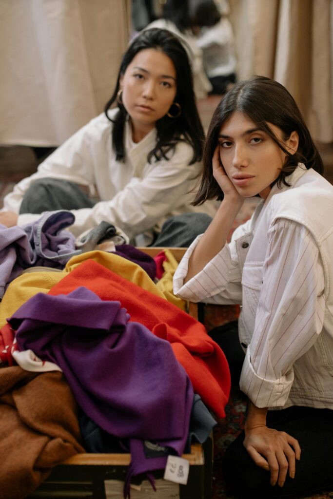 Two women exploring colorful clothes in a thrift store, relaxed and casual setting.